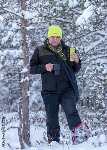  landscape from the swamp, a man drinking tea from a thermos, walking in snowshoes, snow-covered pines in the background, the land is covered with fluffy and white snow, a wonderful winter day 