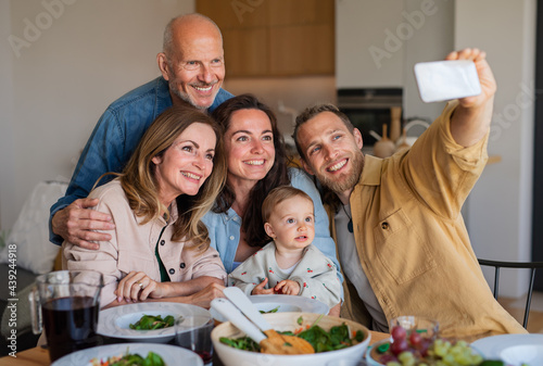 Happy multigeneration family indoors at home eating healthy lunch, taking selfie.