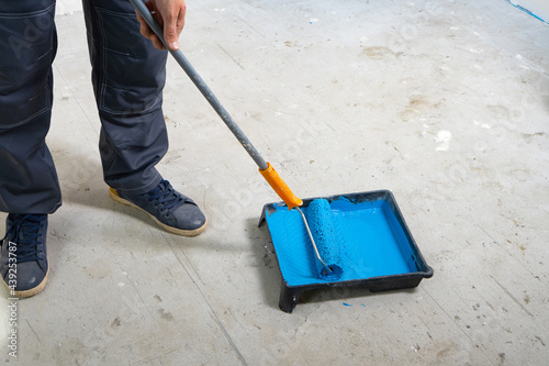 The painter dips his brush in paint bath of blue paint.