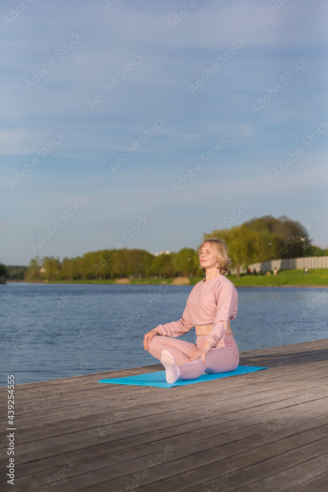 Senior Caucasian Woman During Yoga Relaxing Training On Wooden Stage Near Water Outdoor.