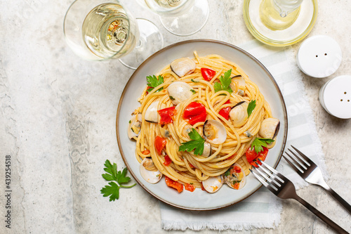 Italian dinner, seafood pasta and white wine. Spaghetti alle vongole or clams, tomato and parsley. Light stone background.
