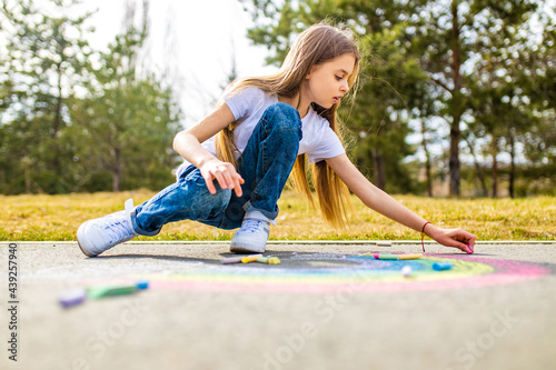 teenage girl drawing a rainbow colored chalk on the asphalt on summer day photo