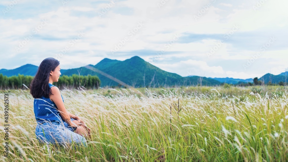 Asian beautiful young woman travel and sitting in meadow flower field landscape background.Concept of travel in summer season at Thailand.