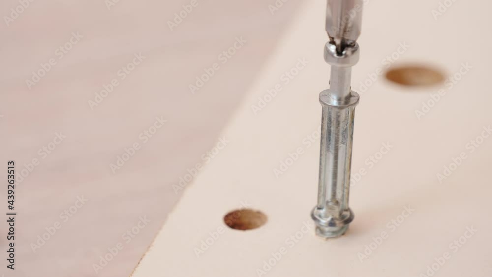 Assembling furniture at home. Mounting screw is screwed into hole board. Closeup of tool in hand. Do it yourself furniture assembly. Assembling furniture at home. Mounting screw is screwed into hole board. Closeup of tool in hand. Do it yourself furniture assembly.