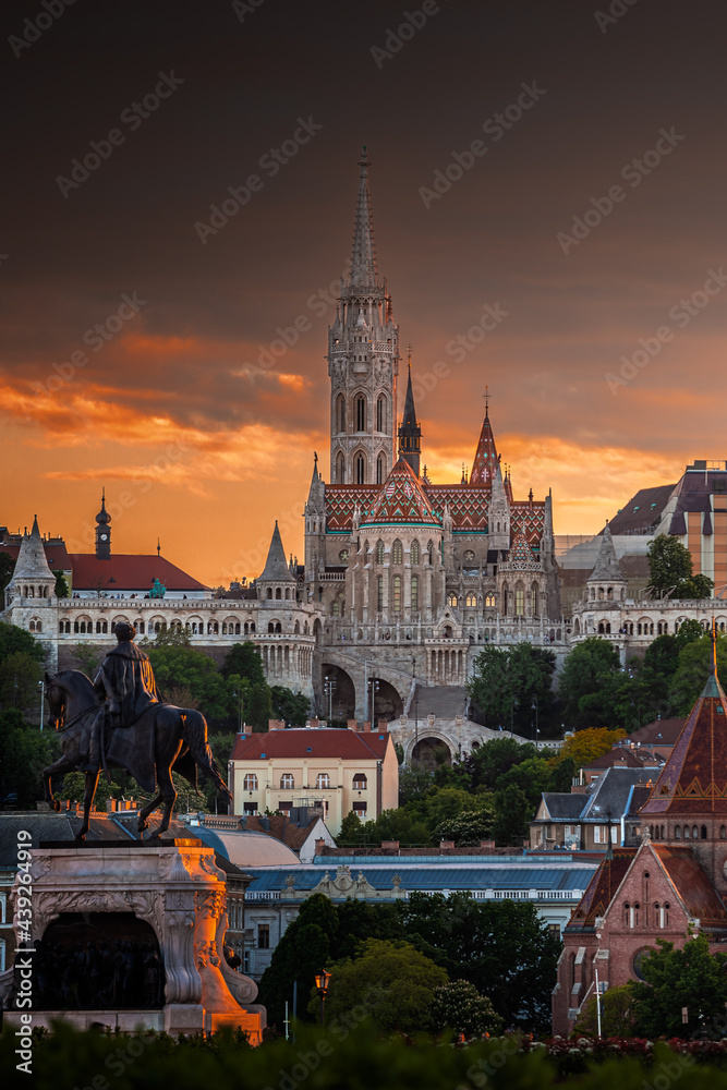 Naklejka premium Budapest, Hungary - St Matthias Church and Fisherman's Bastion (Halaszbastya) with Statue of Gyula Andrassy in foreground and beautiful golden sunset and dramatic sky on a summer afternoon