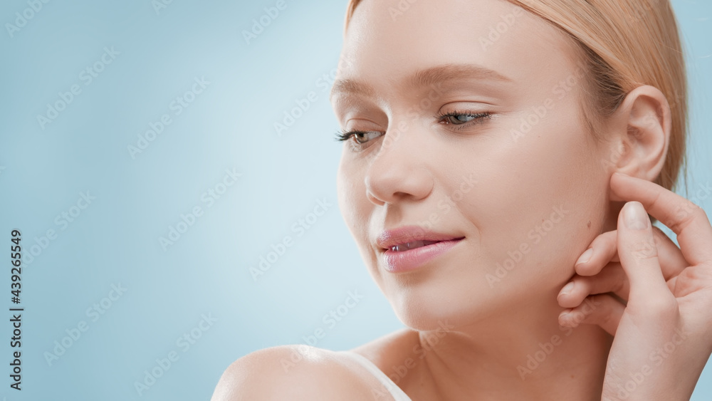 Young fit attractive Caucasian blond woman in white top turns head to the camera touching jaw line and smiling wide against blue ripple background | Moisturizer advertisement Young fit attractive Caucasian blond woman in white top turns head to the camera touching jaw line and smiling wide against blue ripple background | Moisturizer advertisement