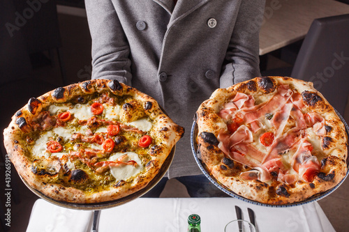 Due pizze napoletane sorrette da un cameriere pronte per essere servite