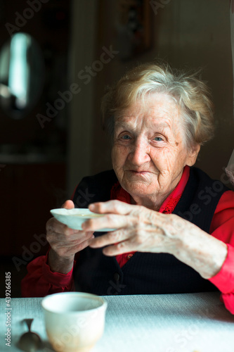 An old woman sits drinking tea, a portrait of grandmother in her home.