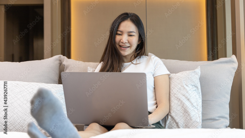 Asian woman uses laptop on bed in modern bedroom at home after she wakes up in the morning, Entertaining or relaxing using laptop technology, Wake-up activities, Happy lifestyle. Asian woman uses laptop on bed in modern bedroom at home after she wakes up in the morning, Entertaining or relaxing using laptop technology, Wake-up activities, Happy lifestyle.