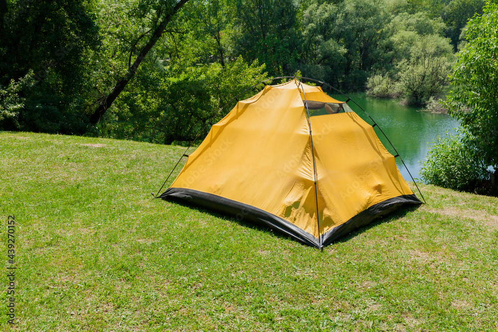 Yellow tent on a grass hill by the lake ready for camping 