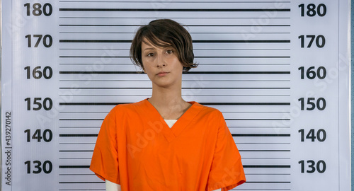Arrested young woman posing in an orange suit for a mugshot photo