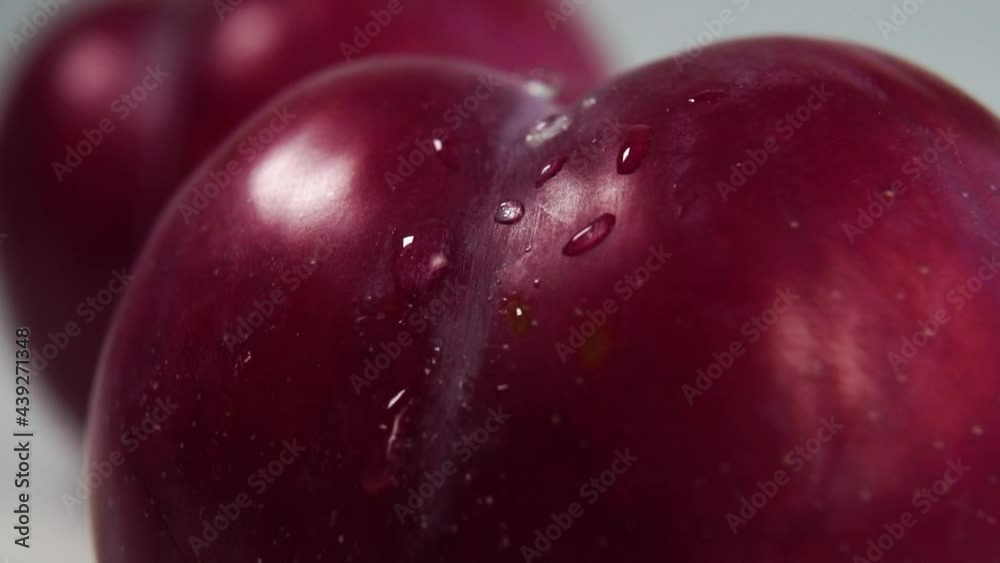 Drops of pure water fall on a ripe plum in slow motion. Macro shot