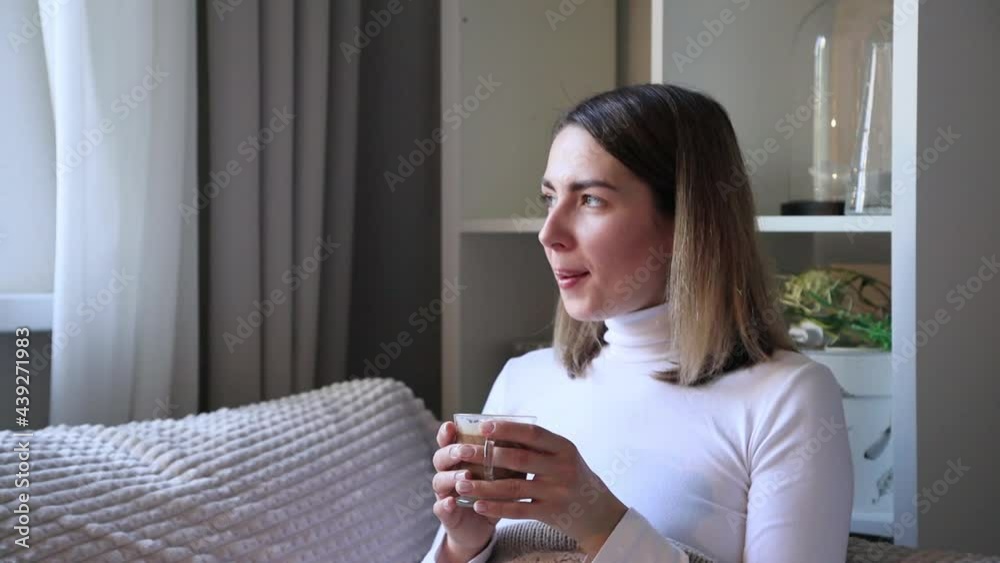 White-skinned girl lies under the covers and drinks coffee and looks out the window. European white-skinned girl is drinking coffee and smiling while looking out the window. White-skinned girl lies under the covers and drinks coffee and looks out the window. European white-skinned girl is drinking coffee and smiling while looking out the window.