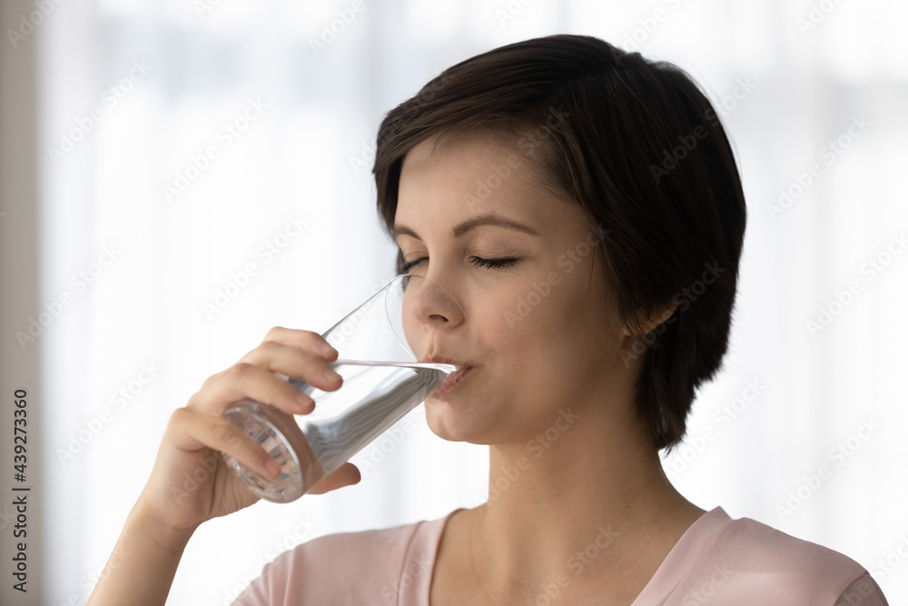 Head shot beautiful dehydrated young woman drinking pure mineral water, holding glass, close up of attractive female enjoying fresh still water with closed eyes, healthy lifestyle and daily habit Head shot beautiful dehydrated young woman drinking pure mineral water, holding glass, close up of attractive female enjoying fresh still water with closed eyes, healthy lifestyle and daily habit