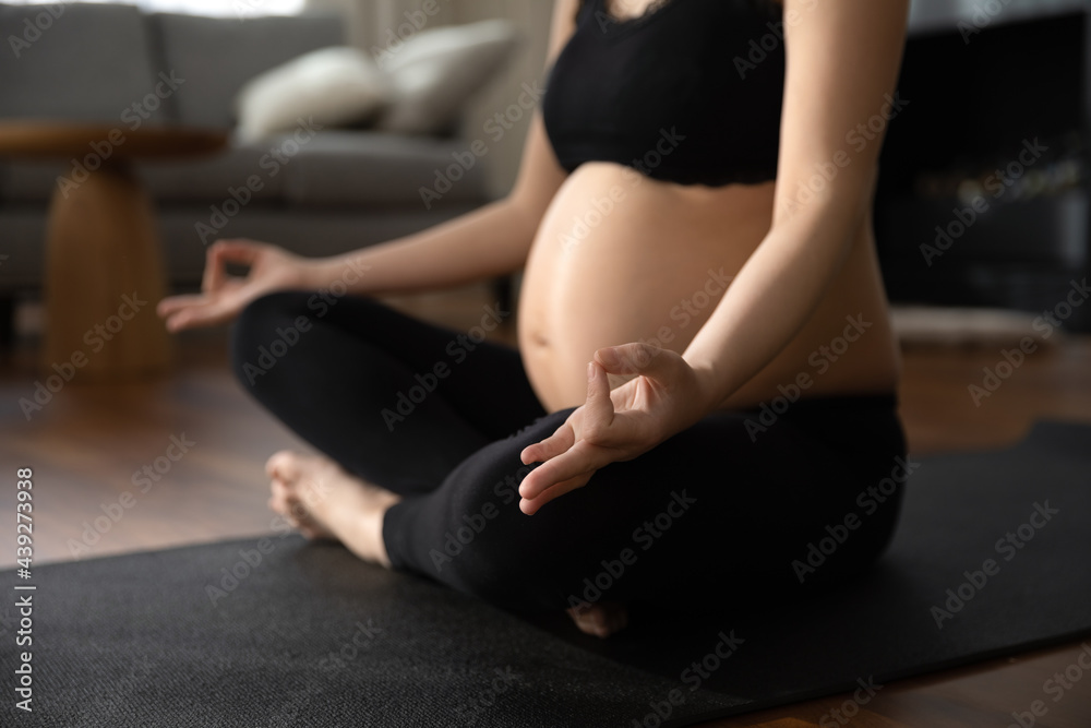 Close up pregnant woman in black sportswear practicing yoga, meditating, sitting in lotus pose on mat, young future mom training, doing exercises, healthy lifestyle and gymnastics during pregnancy