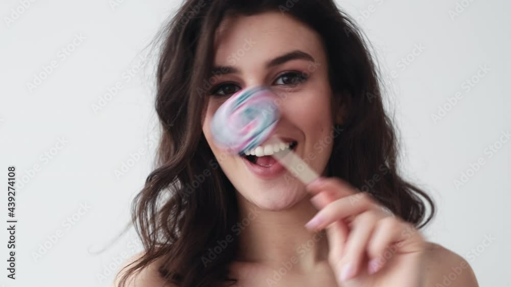Sweet beauty. Lip augmentation. Aesthetic cosmetology. Playful fun brunette woman with pretty face white toothy smile posing with colorful lollipop candy isolated on light.