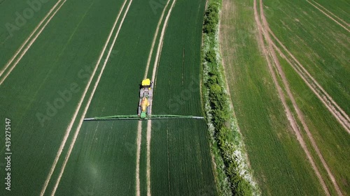 A stationary drone shot of a tractor working and spraying his crops whilst they drive off. Picturesque green fields surround it. photo