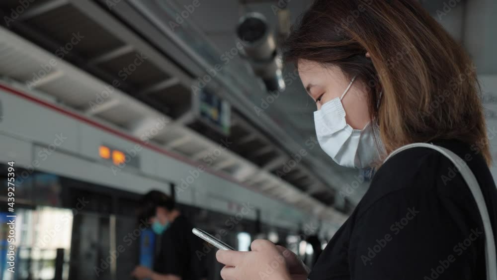 Asian woman wearing face mask using mobile phone. She is waiting for the train to go to work on the platform station. New normal lifestyle in city concept Asian woman wearing face mask using mobile phone. She is waiting for the train to go to work on the platform station. New normal lifestyle in city concept