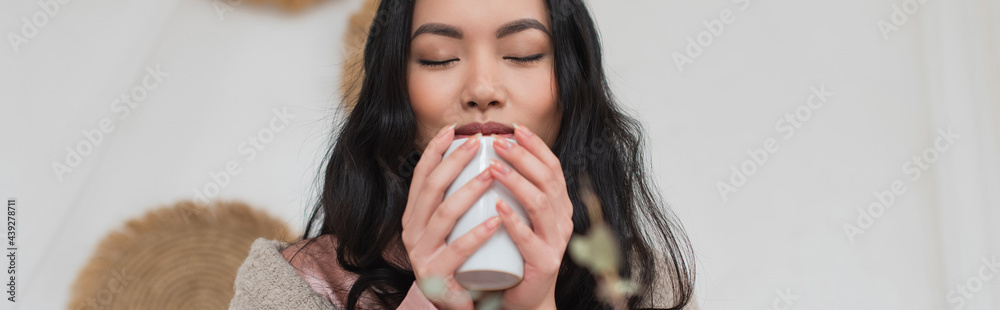 portrait of young asian woman holding cup of coffee in hands and enjoying aroma in bedroom, banner portrait of young asian woman holding cup of coffee in hands and enjoying aroma in bedroom, banner