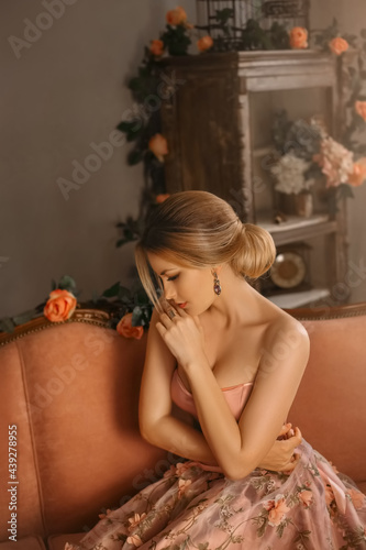fantasy woman in medieval pink evening sexy dress with bare shoulders, spring flowers on skirt. Fashion model girl sitting on sofa. beauty face. queen in vintage corset clothes. Elegant bun blond hair