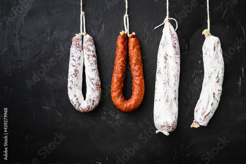 Spanish salami, fuet and salchichon sausages hang from a rack on black surface