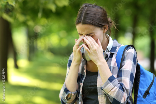 Student suffering allergy symptoms scratching eyes in a park