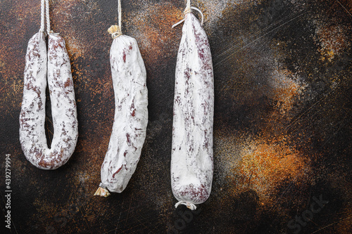 Dry cured chorizo and fuet salami sausages hanging on dark background