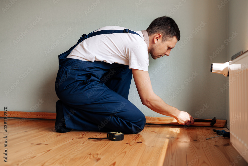 Fototapeta premium To make repairs. Installing a new skirting board. a man makes repairs in a room