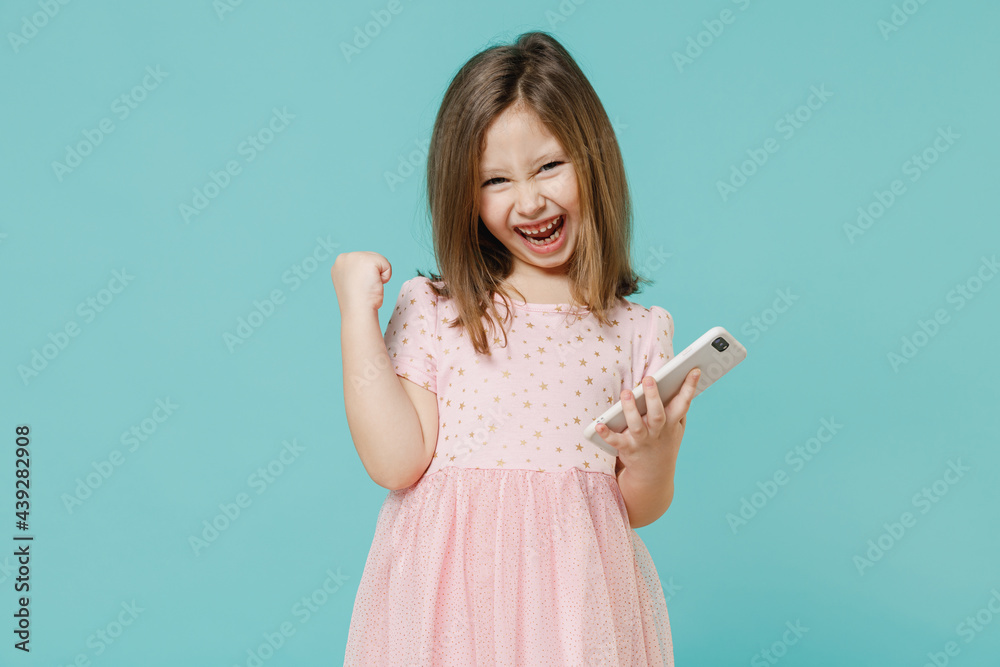 Little fun cute kid girl 5-6 years old wears pink dress hold in hand using mobile cell phone isolated on pastel blue color background child studio portrait. Mother's Day love family lifestyle concept. Little fun cute kid girl 5-6 years old wears pink dress hold in hand using mobile cell phone isolated on pastel blue color background child studio portrait. Mother's Day love family lifestyle concept.