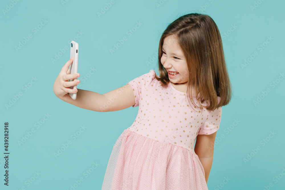 Little fun kid girl 5-6 years old wear pink dress doing selfie shot on mobile phone post photo on social network isolated on pastel blue color background child studio Mother's Day love family concept Little fun kid girl 5-6 years old wear pink dress doing selfie shot on mobile phone post photo on social network isolated on pastel blue color background child studio Mother's Day love family concept