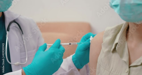 Doctors wearing protective clothing and masks are vaccinating. Doctor holding syringe and using cotton before make injection to patient in medical mask. Covid-19 or coronavirus vaccine.