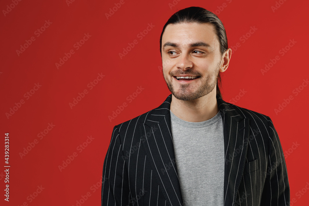Young smiling surprised businessman latin man 20s long hair ponytail wear black striped jacket grey shirt looking aside isolated on red color background studio portrait Concept of people lifestyle Young smiling surprised businessman latin man 20s long hair ponytail wear black striped jacket grey shirt looking aside isolated on red color background studio portrait Concept of people lifestyle