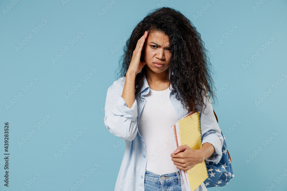 Young sad exhausted tired ill african american girl teen student in denim clothes backpack hold books prop up forehead isolated on blue background Education in high school university college concept. Young sad exhausted tired ill african american girl teen student in denim clothes backpack hold books prop up forehead isolated on blue background Education in high school university college concept.