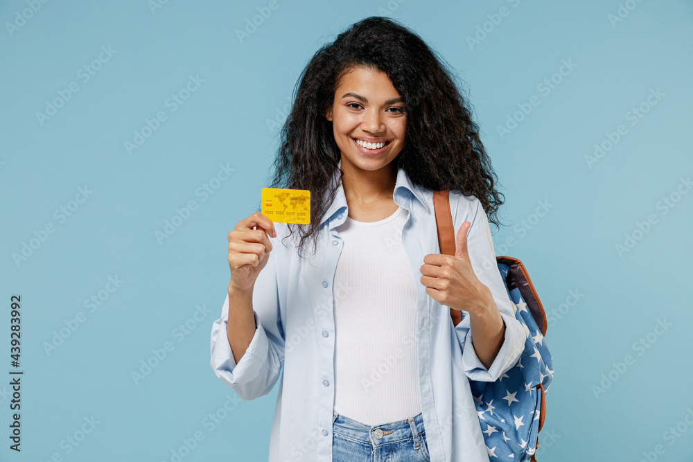 Young happy african american girl teen student wear denim clothes backpack hold credit bank card isolated on blue color background studio portrait. Education in high school university college concept Young happy african american girl teen student wear denim clothes backpack hold credit bank card isolated on blue color background studio portrait. Education in high school university college concept
