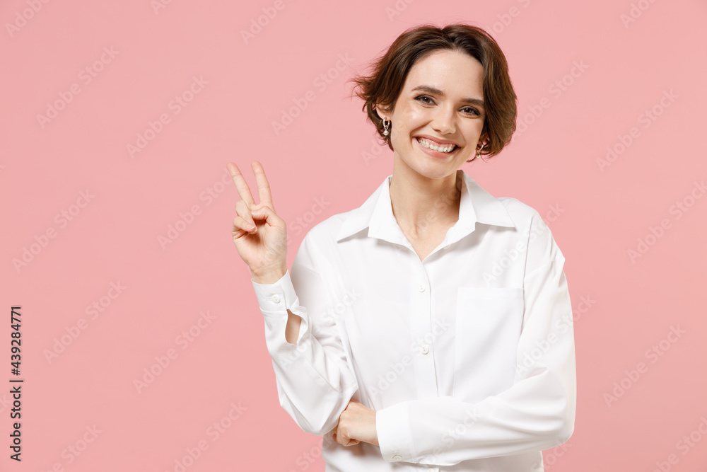 Young smiling successful employee business woman corporate lawyer 20s in classic formal white shirt work in office show victory v-sign gesture isolated on pastel pink color background studio portrait. Young smiling successful employee business woman corporate lawyer 20s in classic formal white shirt work in office show victory v-sign gesture isolated on pastel pink color background studio portrait.