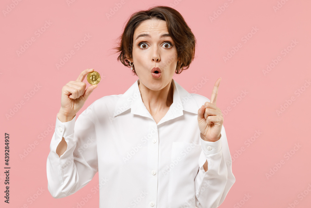 Young employee business secretary woman corporate lawyer in classic formal white shirt work in office holding bitcoin coin currency point index finger with new idea isolated on pastel pink background