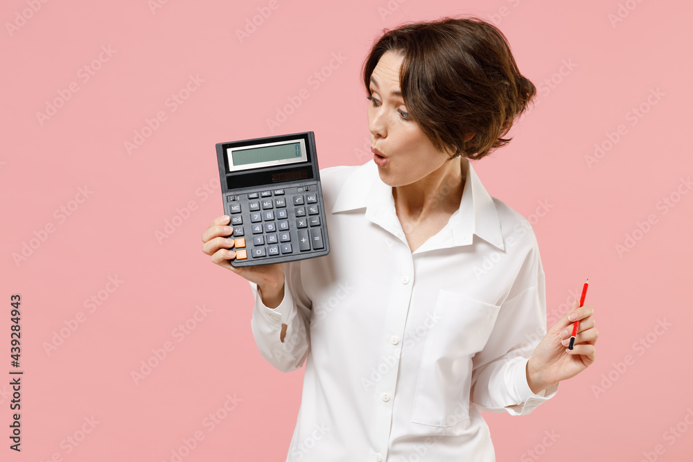 Young surprised successful employee business secretary woman corporate lawyer in classic formal white shirt work in office hold in hands calculator isolated on pastel pink background studio portrait Young surprised successful employee business secretary woman corporate lawyer in classic formal white shirt work in office hold in hands calculator isolated on pastel pink background studio portrait