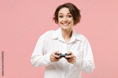 Young excited fun happy employee business secretary woman corporate lawyer in classic formal white shirt work in office play pc game with joystick console isolated on pastel pink background studio