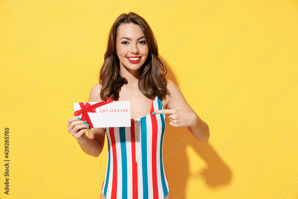 Happy young woman slim body wear striped red blue swimsuit hold gift certificate coupon voucher store card isolated on vivid yellow color background studio. Summer hotel pool sea rest sun tan concept. Happy young woman slim body wear striped red blue swimsuit hold gift certificate coupon voucher store card isolated on vivid yellow color background studio. Summer hotel pool sea rest sun tan concept.