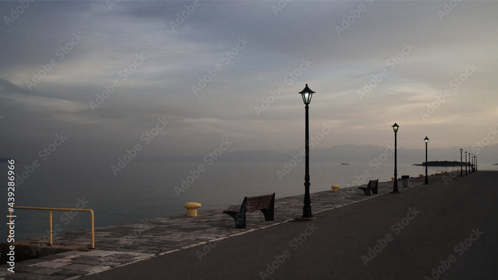 a traditional street light in front of a bench on the pier by the sea at sunset, Itea, Greece
