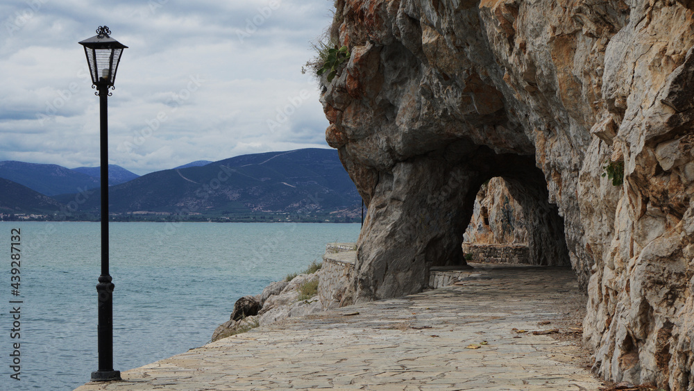 a traditional street light on the coastal sidewalk next to the caves of Akronafplia by the sea, Nafplio, Greece