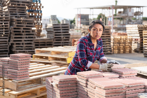 Female warehouse employee puts paving slabs on a pallet