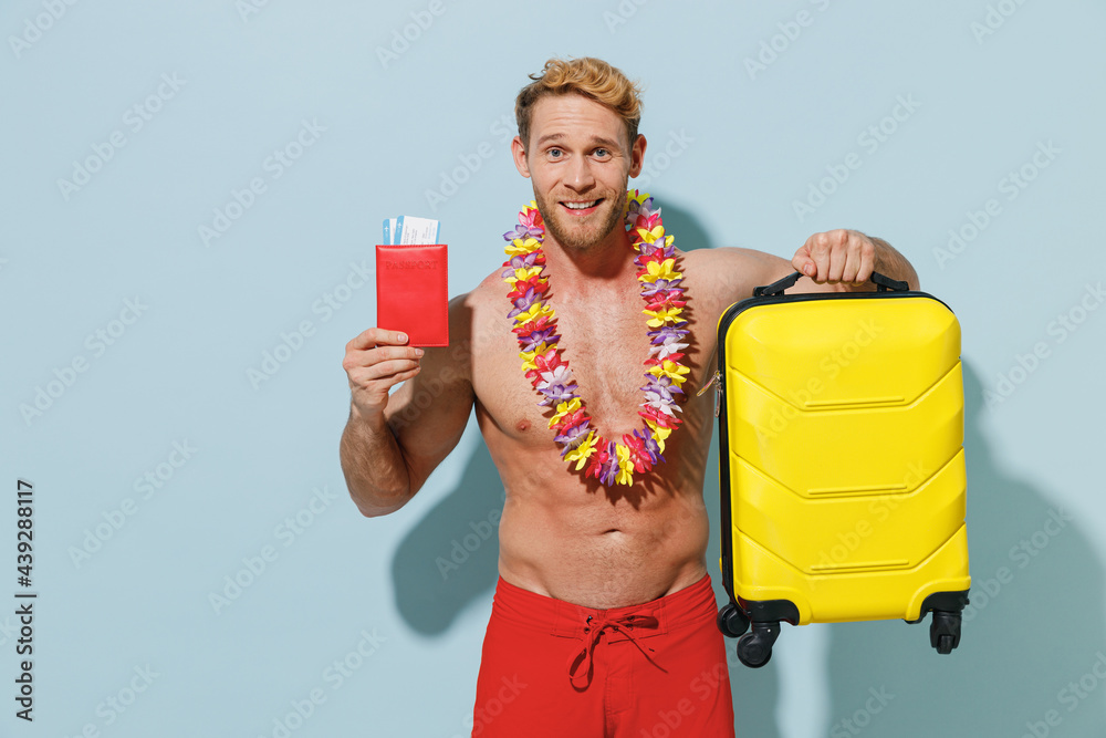 Traveler tourist young man in shorts swimsuit hold passport ticket suitcase bag hawaii lei isolated on blue background. Passenger travel abroad on weekends getaway Air flight sea rest journey concept