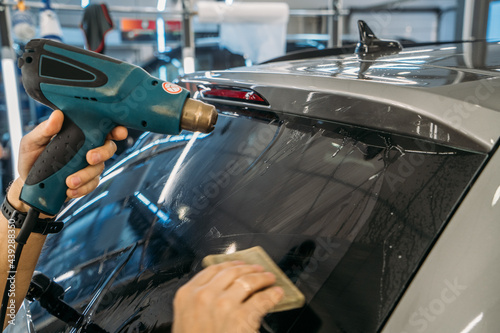 Professional detailer warms up tint film with industrial dryer to apply tinting on car glass, close up.