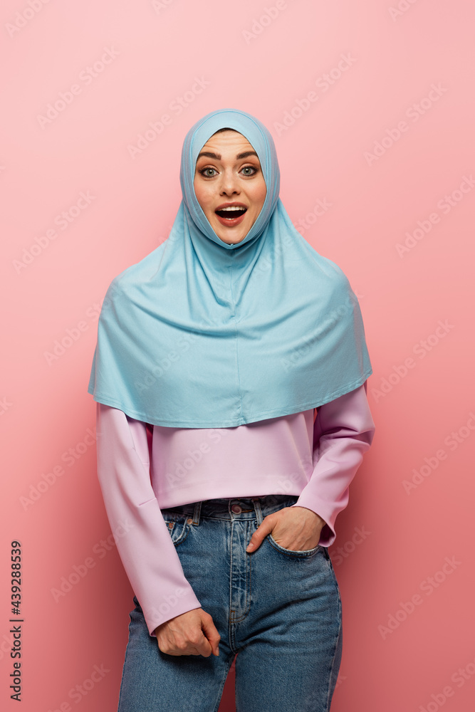 amazed muslim woman in jeans standing with hand in pocket on pink background amazed muslim woman in jeans standing with hand in pocket on pink background