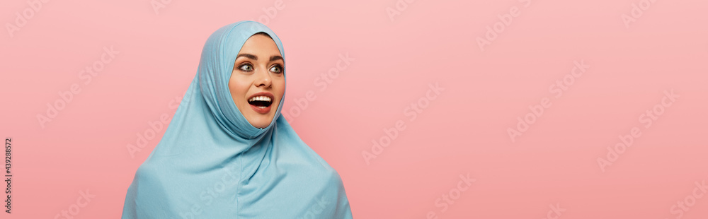 amazed arabian woman in blue hijab looking away isolated on pink, banner amazed arabian woman in blue hijab looking away isolated on pink, banner