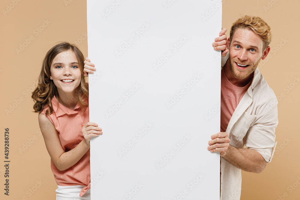 Young fun parent man with child teen girl in casual clothes. Daddy kid daughter hold big white empty blank poster billboard, promotional content, place for text or image isolated on beige background Young fun parent man with child teen girl in casual clothes. Daddy kid daughter hold big white empty blank poster billboard, promotional content, place for text or image isolated on beige background
