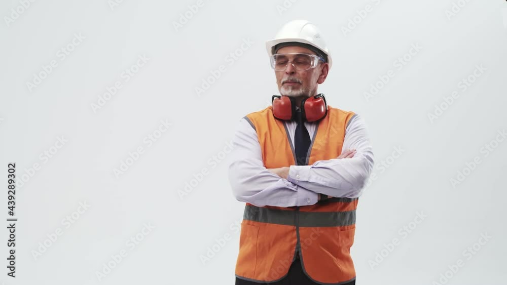 Engineer in vest with headphones around neck and helmet crosses arms on chest. Working adult man crosses arms. Engineer in vest with headphones around neck and helmet crosses arms on chest. Working adult man crosses arms.