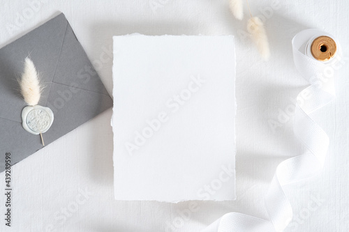Flatlay wedding invitation card, grey envelope with seal wax stamp, dried flowers on pastel white background. Wedding stationery set top view.