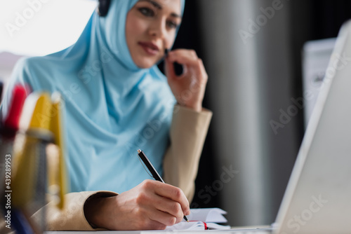 blurred muslim woman writing in notebook while working in call center